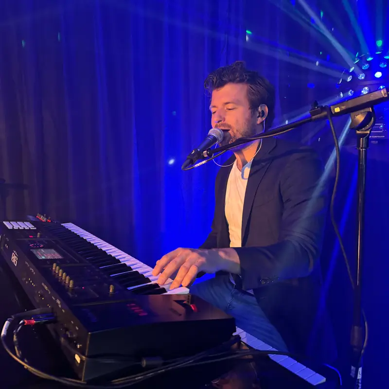 De pianist achter zijn keyboard tijdens een optreden in blauw podiumlicht